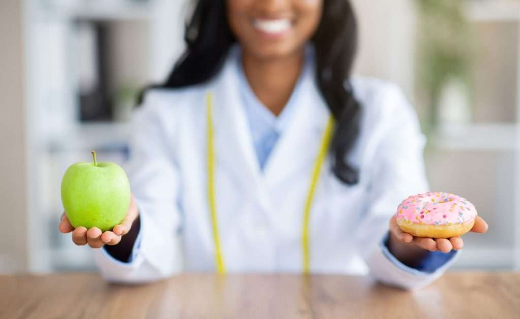 Doctor holding apple and doughnut each hand for preventative care.