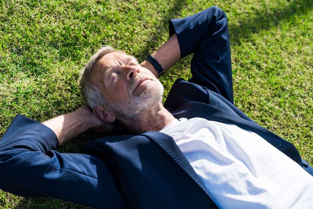 A matured businessman with good geriatric health care lying on the grass.