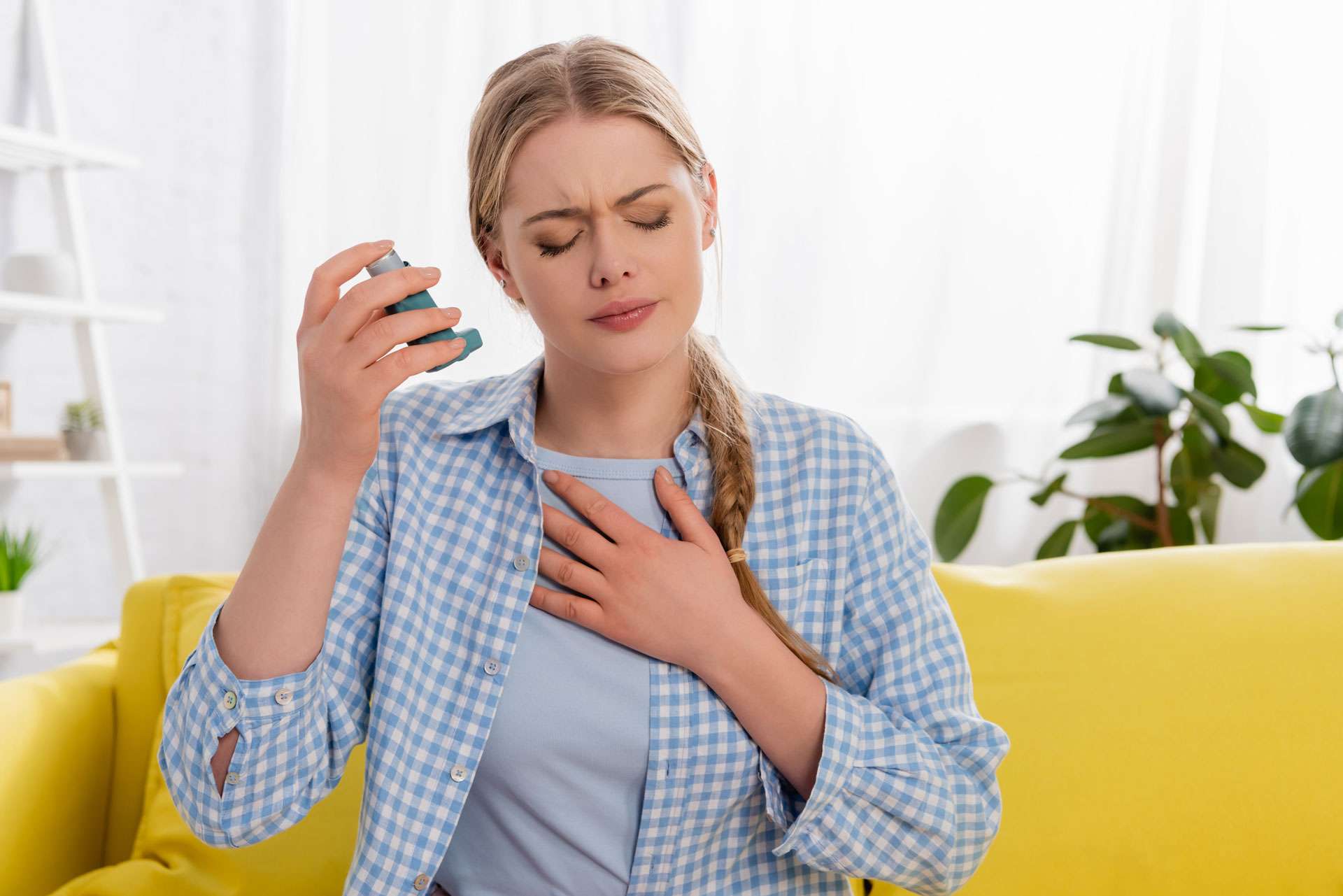 Sick woman holding inhaler in couch.