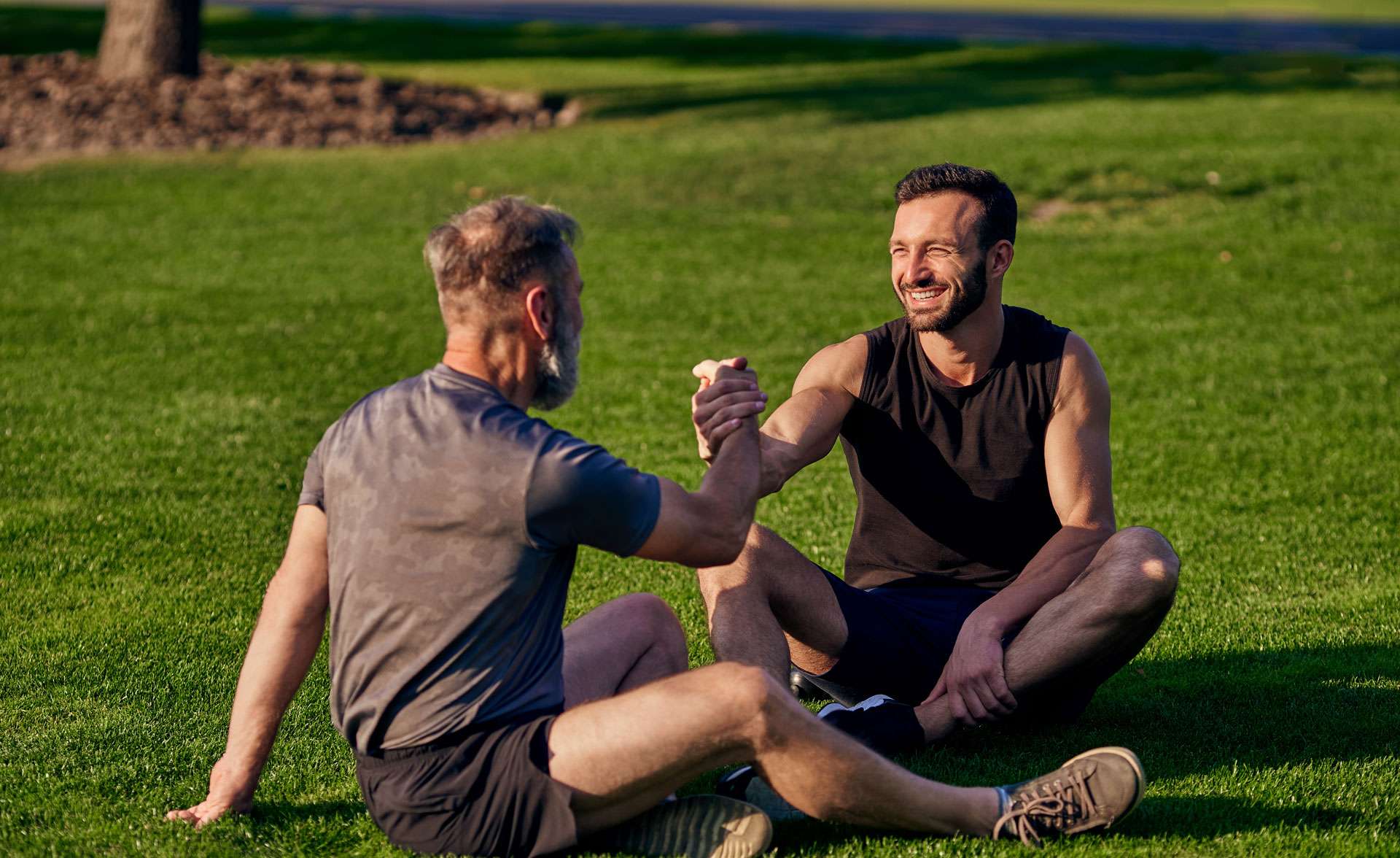 Two men sitting on the grass and having a handshake.
