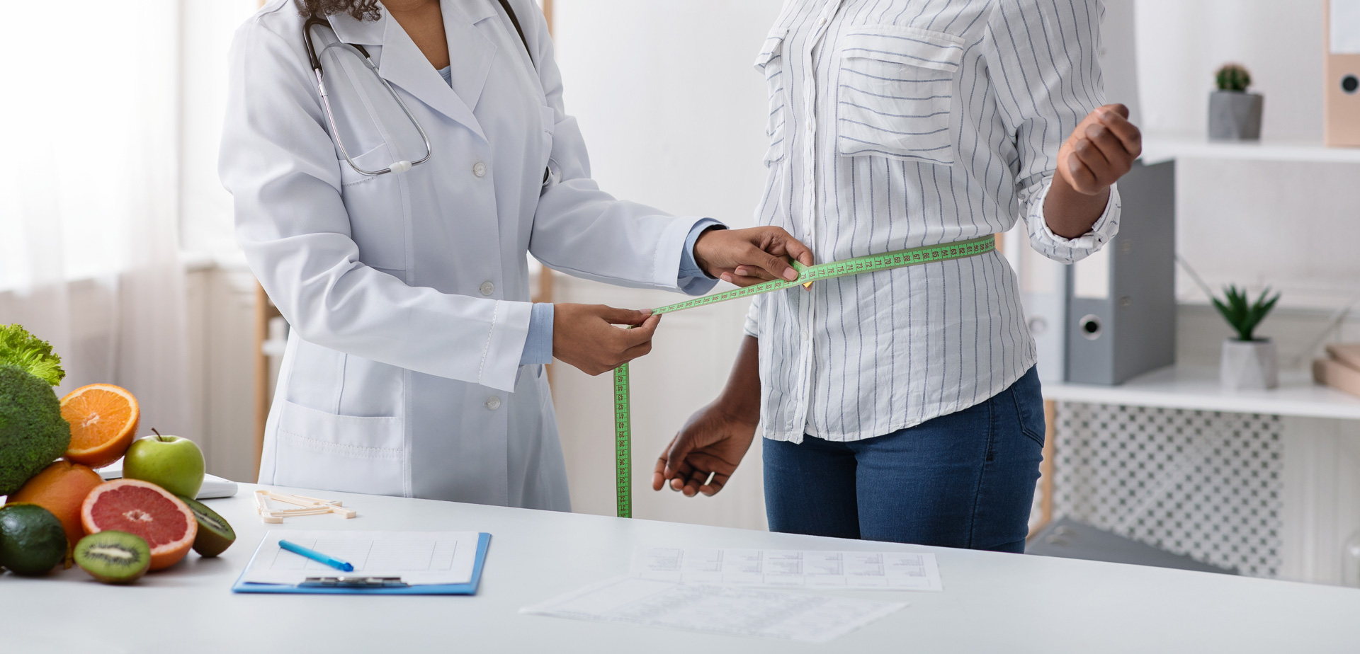 Doctor measures patient waist in office.